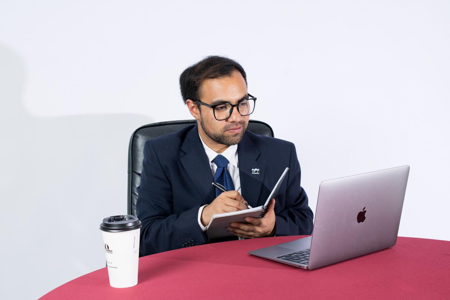 Hombre de negocios en una oficina moderna tomando notas junto a su portátil, ideal para representar el perfil profesional corporativo.