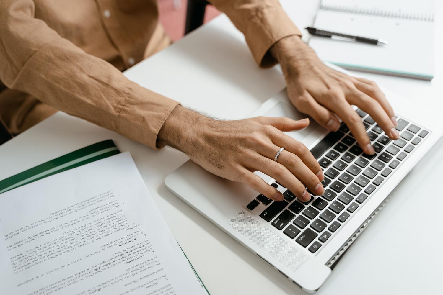 Primer plano de manos escribiendo en un teclado con documentos al lado, simbolizando la atención al detalle en el formato del texto.