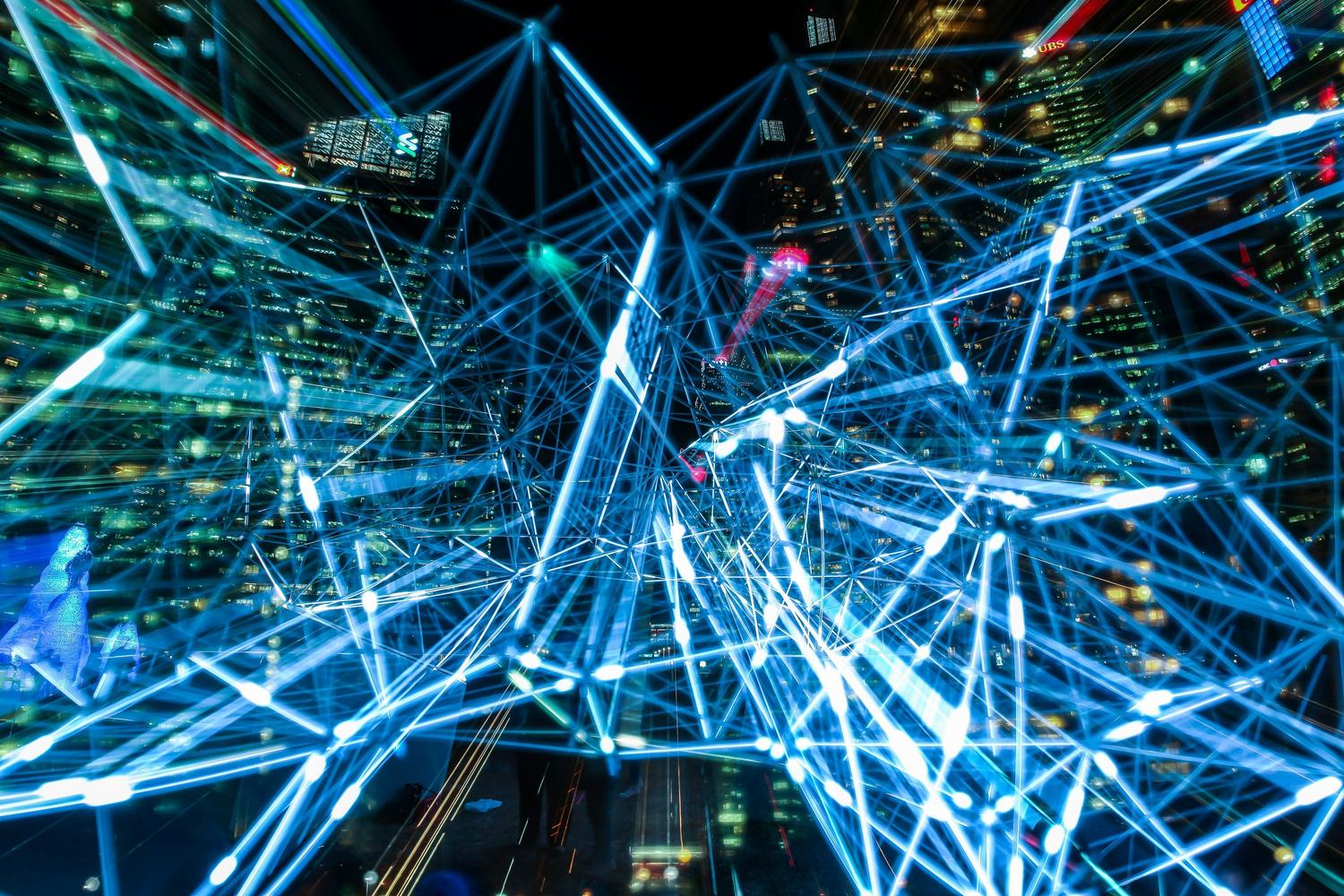 Representación de una red de datos interconectada con flujos de luz azul neón sobre un fondo urbano nocturno, ideal para ilustrar la infraestructura de datos.