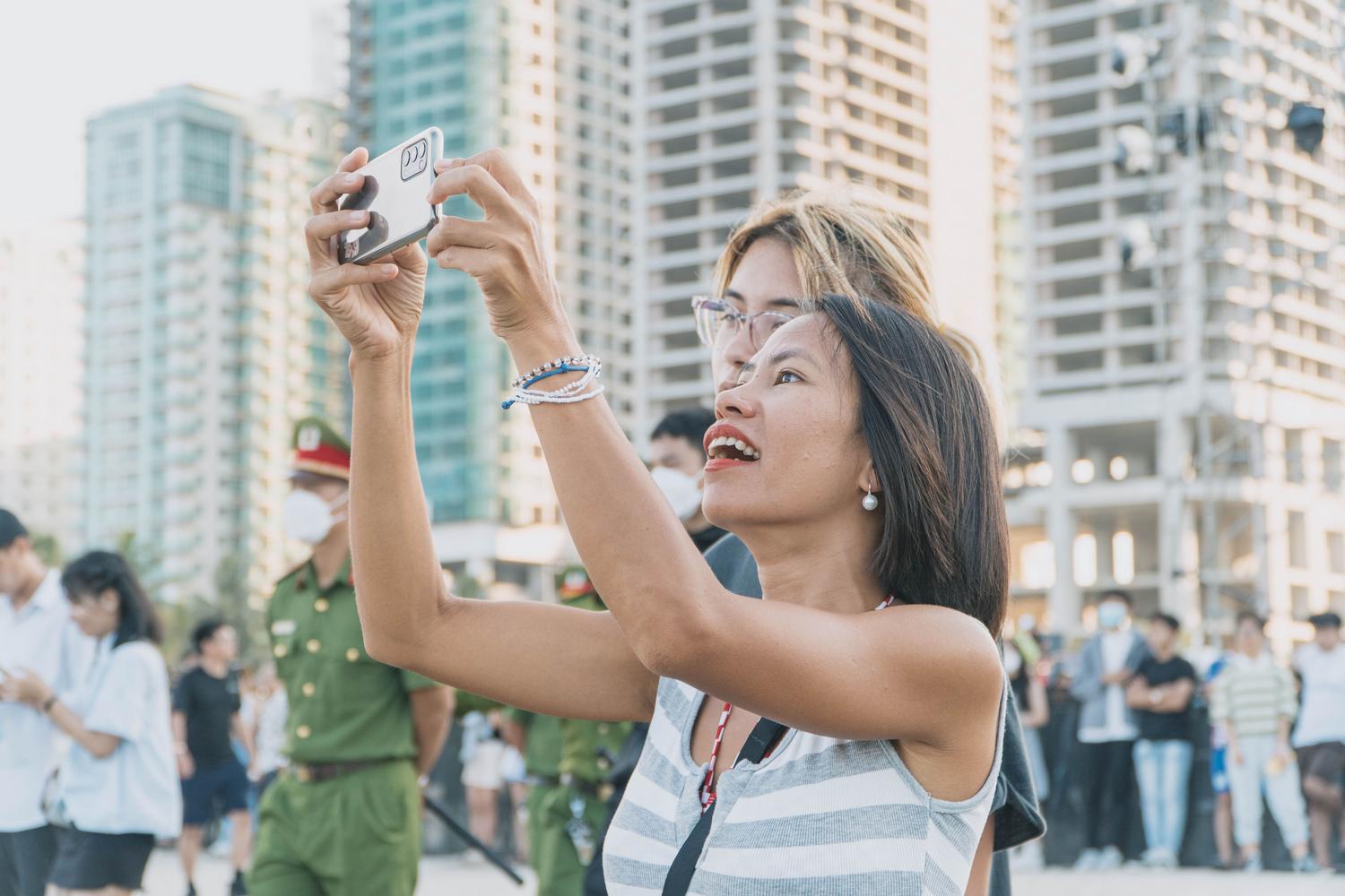 Una mujer asiática utilizando alegremente su smartphone en un entorno urbano moderno y bullicioso.