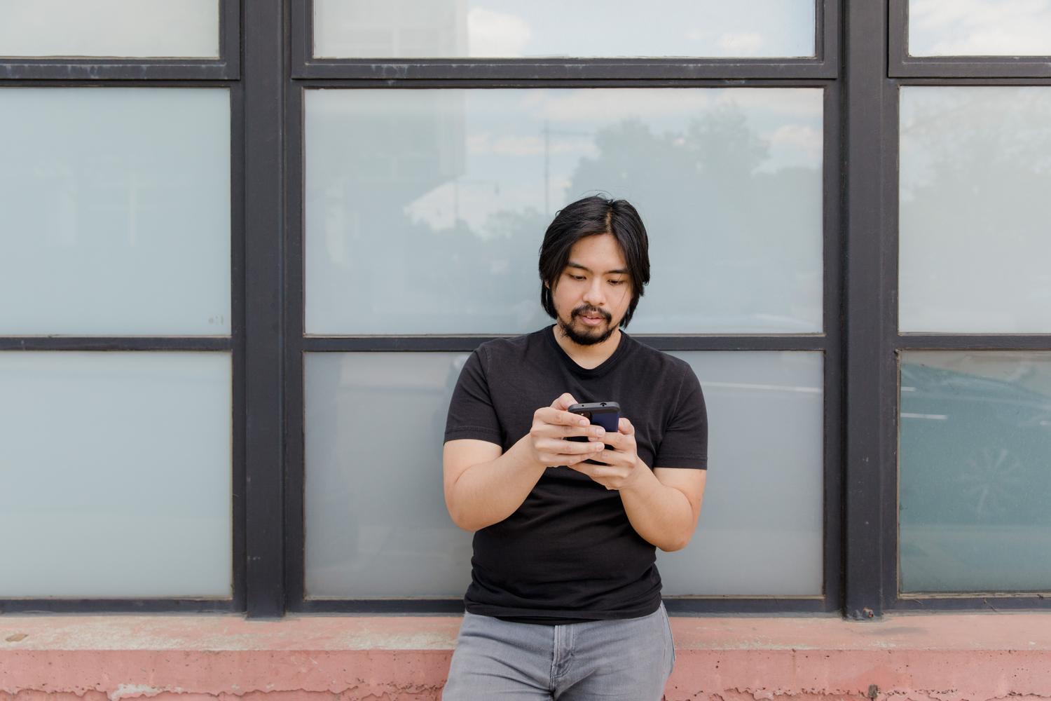 Hombre asiático usando su teléfono móvil frente a un ventanal en una ciudad moderna.