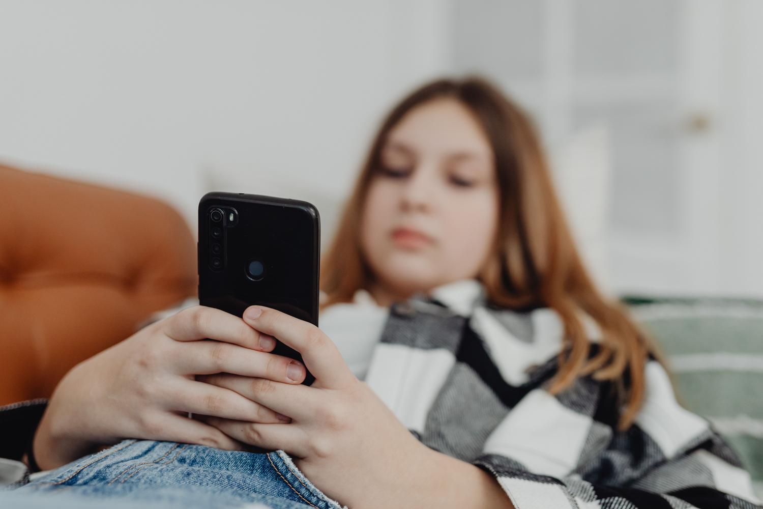 Adolescente usando un smartphone mientras descansa en el sofá, representando el uso cotidiano de dispositivos móviles.