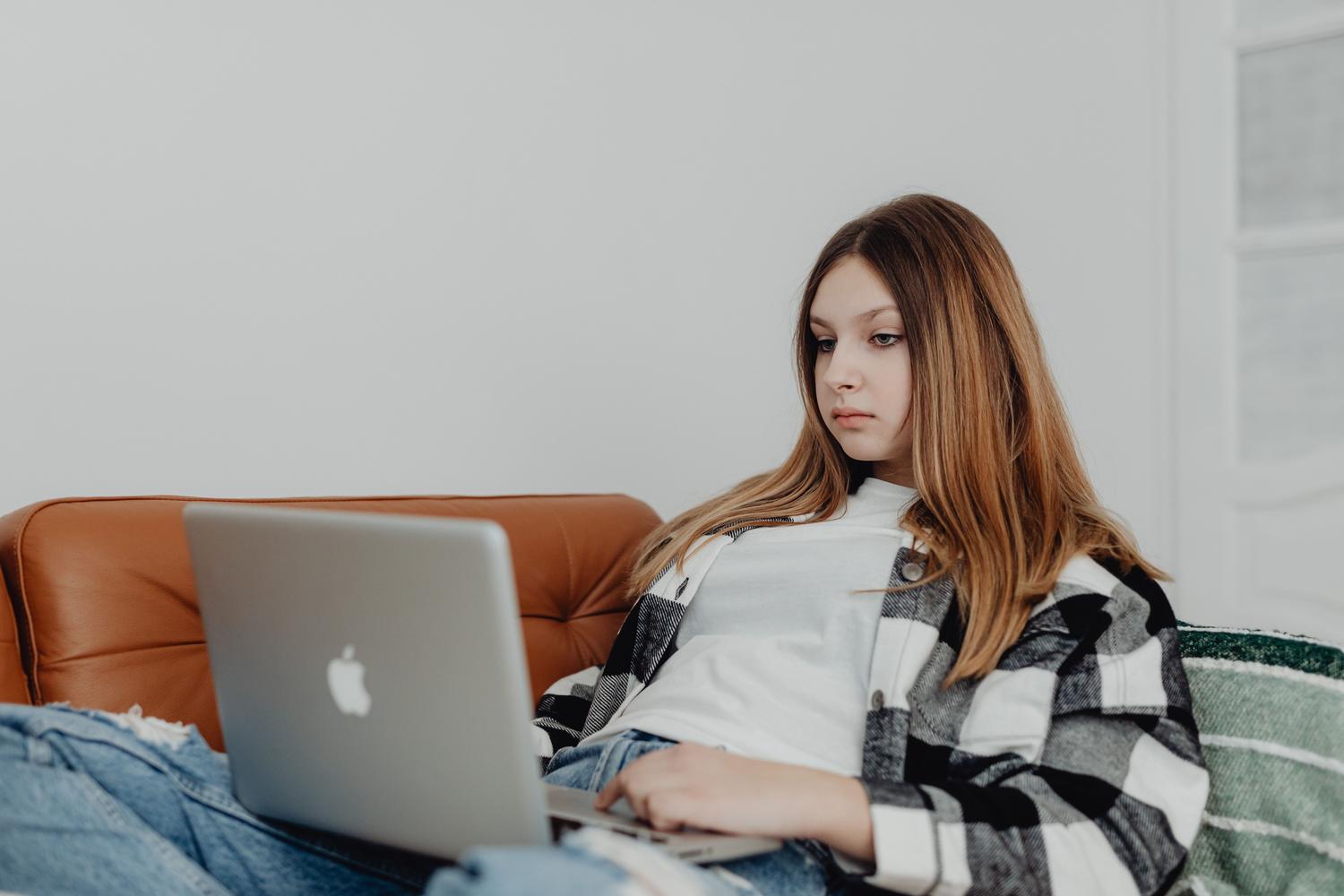 Adolescente concentrada usando un ordenador portátil en el sofá, ilustrando la gestión de controles parentales en PC.