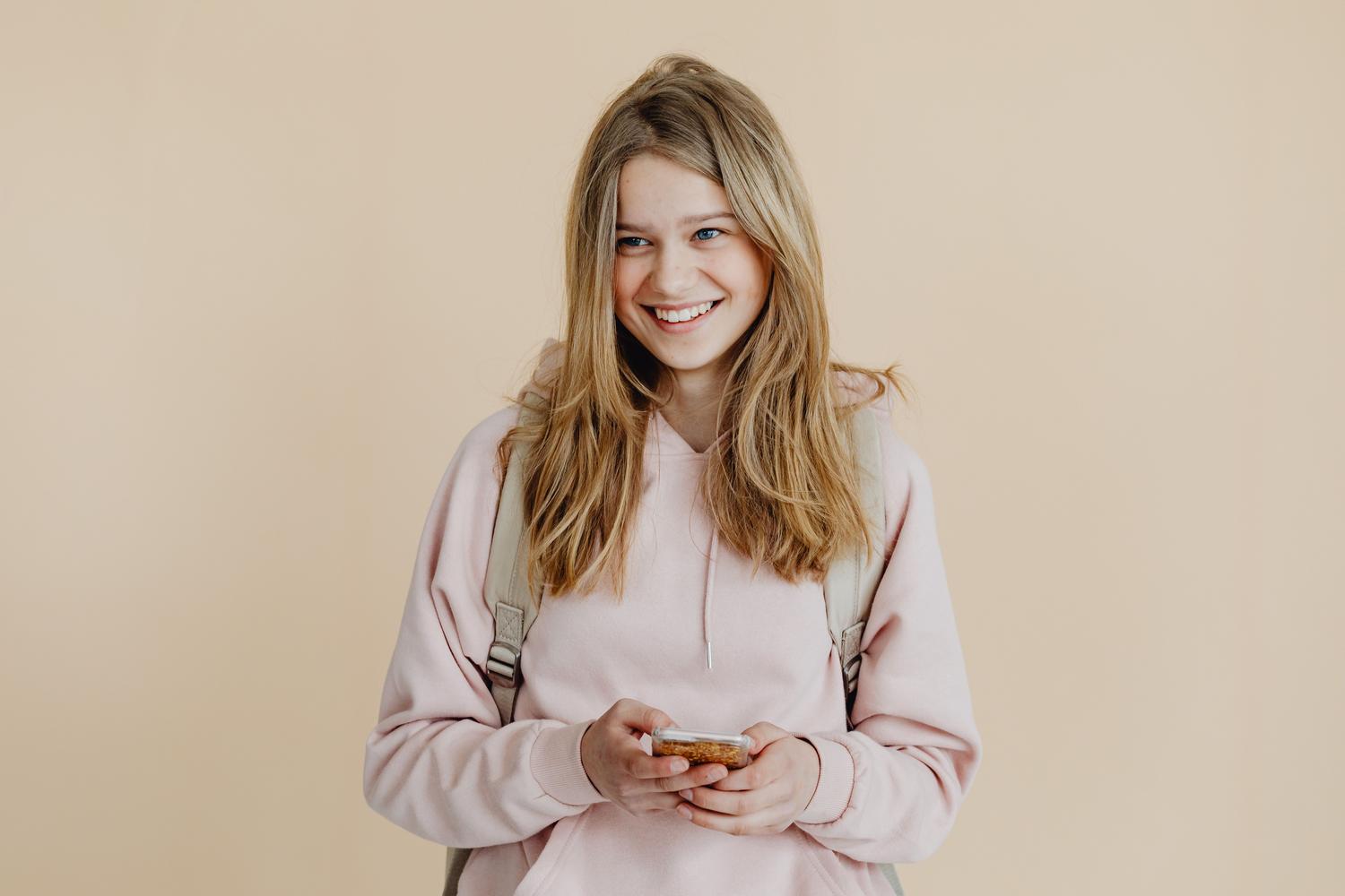 Adolescente sonriendo mientras usa su teléfono, reflejando la confianza y la madurez alcanzada tras la retirada de restricciones.