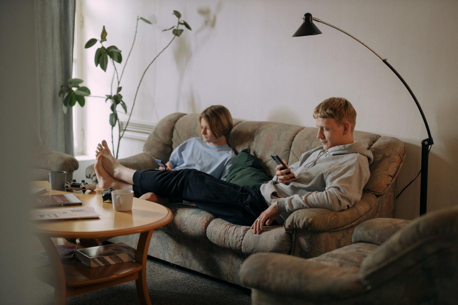 Pareja joven relajada en el sofá usando sus teléfonos móviles en un ambiente hogareño de consumo de streaming.