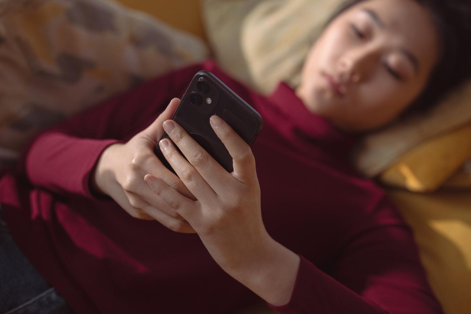 Mujer joven tumbada en un sofá usando un smartphone con las manos en primer plano, ajustando la configuración de la aplicación.