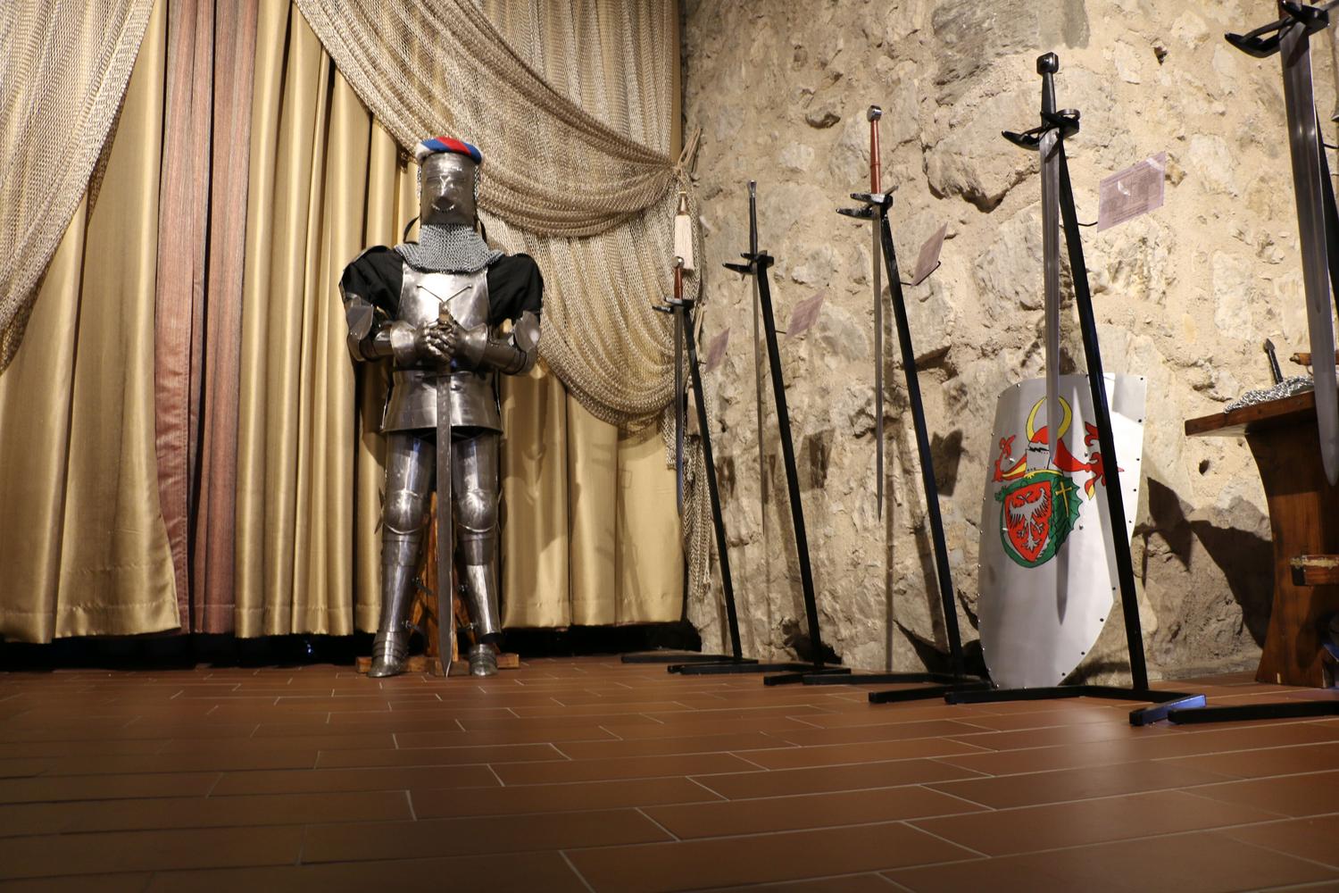Exhibición de armadura medieval y espadas en un entorno histórico, ideal para ilustrar el equipo de las Escuelas de Brujos.