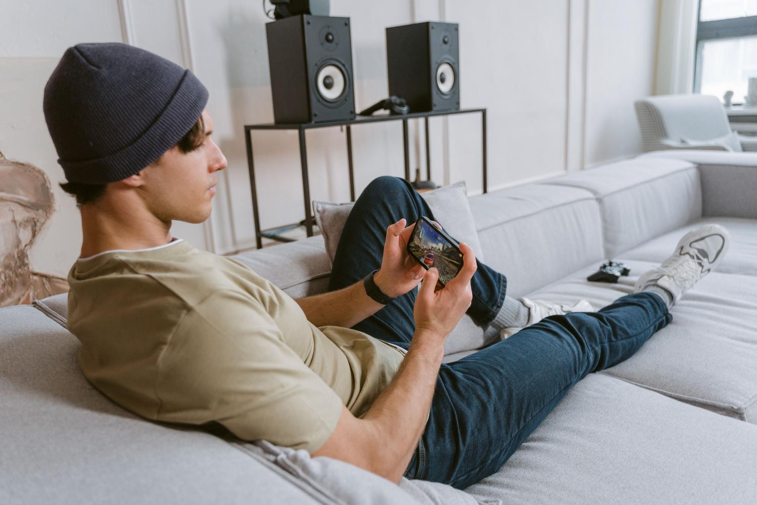 Persona relajada en un sofá jugando con su móvil, mostrando la portabilidad y comodidad de llevar la potencia de una PS3 al bolsillo.