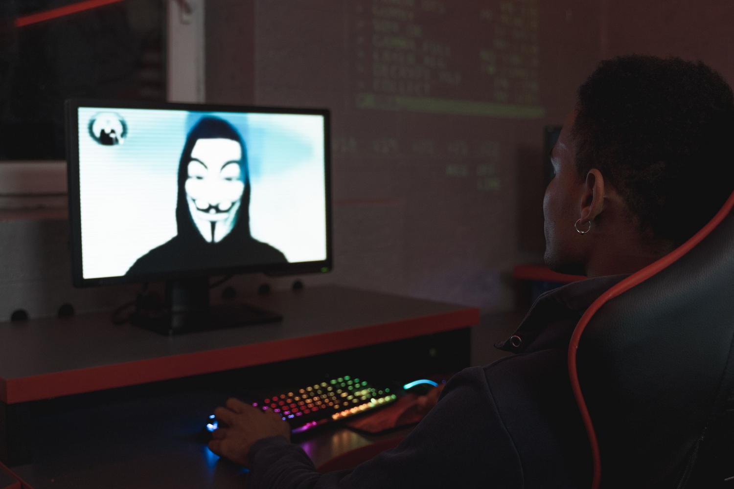 Imagen de un hacker con máscara en una pantalla en un entorno oscuro, representando las amenazas digitales y la vigilancia masiva.