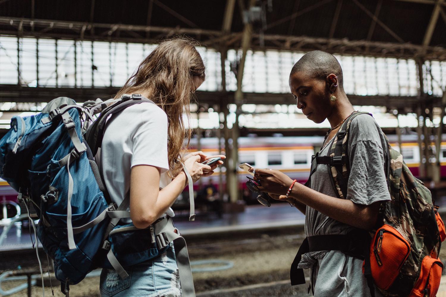 Viajeros consultando sus smartphones en una estación de tren, representando el riesgo de pérdida durante viajes.