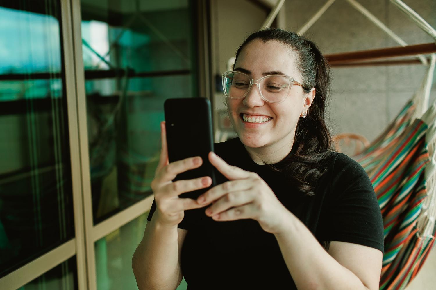 Mujer joven sonriendo mientras interactúa con su smartphone en un ambiente relajado, representando la conexión social a través de WhatsApp.