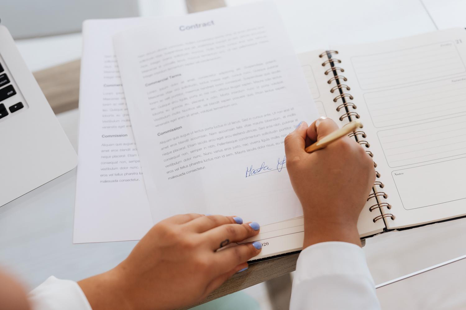 Detalle de unas manos firmando un documento legal sobre un escritorio, representando la firma del contrato de donación necesario para el trámite.