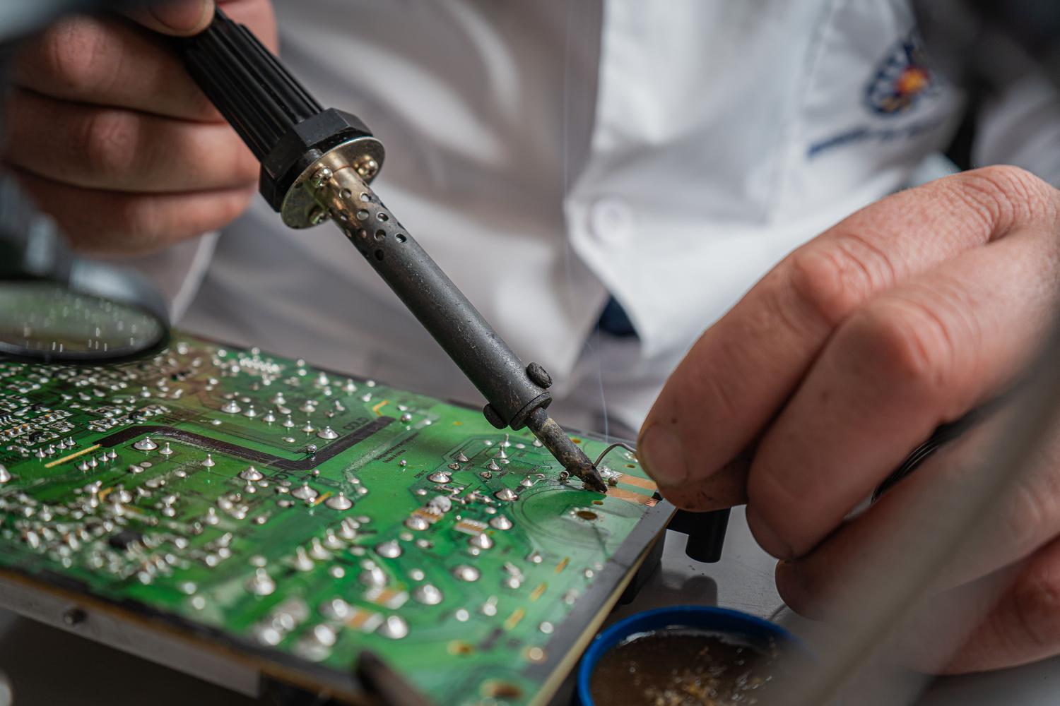 Primer plano detallado de un técnico realizando una soldadura de precisión en una placa de circuito impreso durante la reparación de un dispositivo LED.