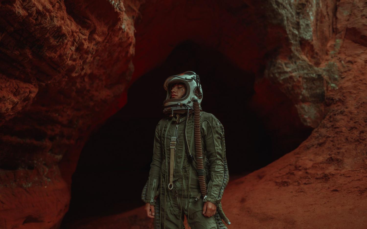 Astronauta solitario explorando una cueva alienígena de tonos rojizos y oscuros, representando la fragilidad y el aislamiento en un entorno hostil.