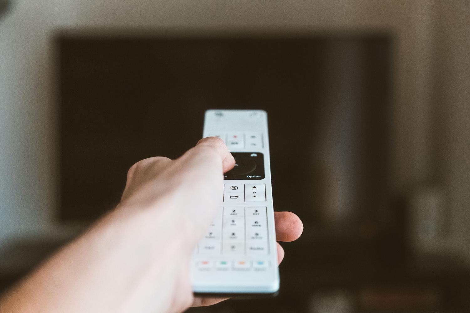 Primer plano de una mano operando el mando a distancia de un televisor, representando la navegación por menús y ajustes de configuración.