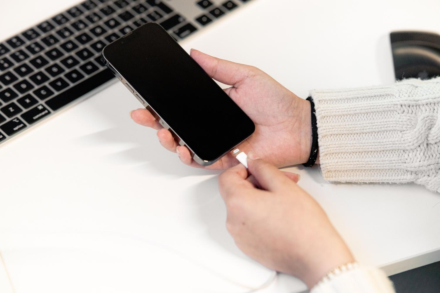 Persona conectando un smartphone a un ordenador portátil mediante un cable USB para transferir archivos.