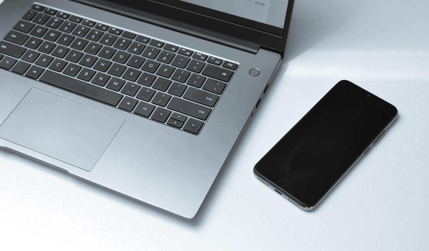 Vista cenital de un ordenador portátil y un teléfono móvil en un escritorio minimalista, simbolizando la conectividad general entre dispositivos.