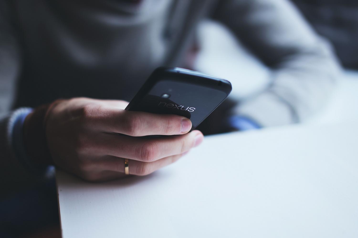 Persona sosteniendo un smartphone sobre una mesa blanca, vista detallada del dispositivo.