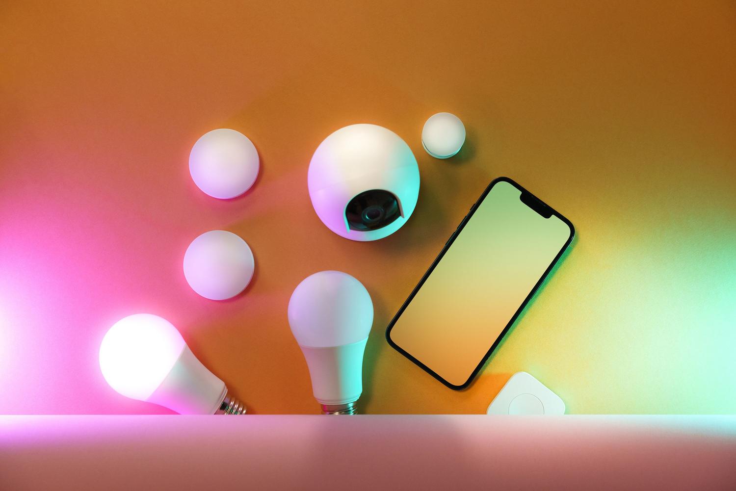 Smartphone junto a bombillas inteligentes y otros dispositivos domóticos, ilustrando la configuración digital y el control mediante aplicaciones.