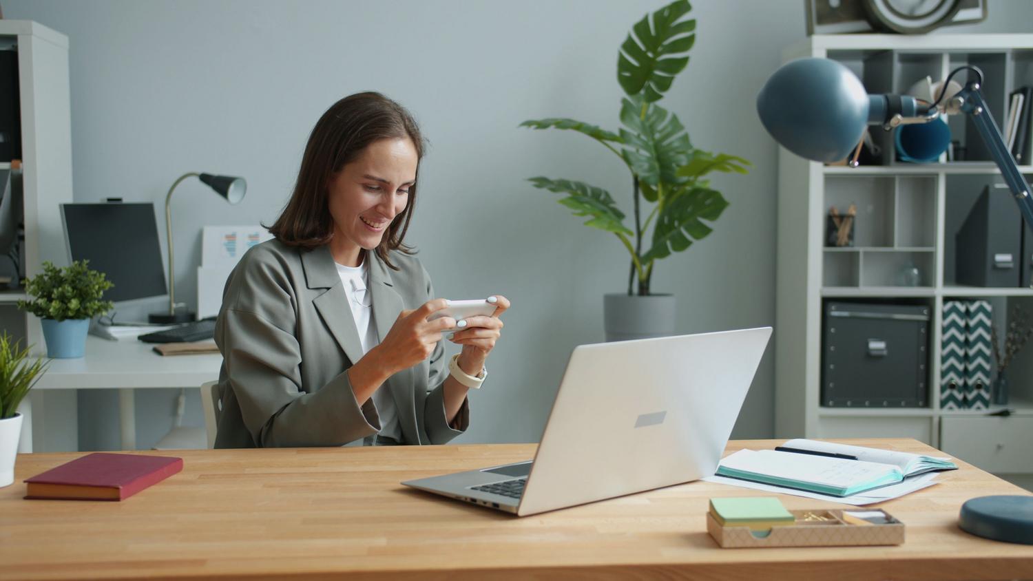 Mujer en su oficina en casa utilizando simultáneamente un ordenador portátil y un móvil, ilustrando la gestión personal de datos.