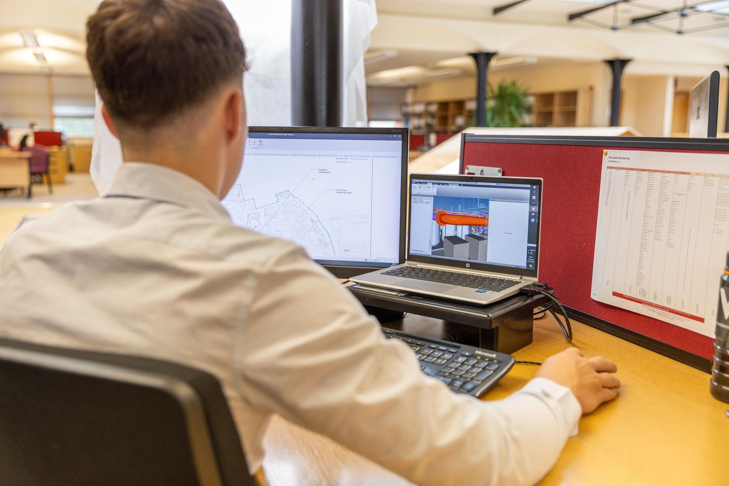 Ingeniero enfocado en el diseño técnico utilizando una configuración de monitores duales para planos y modelos 3D.